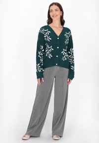 Cárdigan de punto en verde azulado con escote en V y bordado floral blanco, con grandes botones. Combinado con pantalones de pierna ancha grises y zapatos planos en color beige.