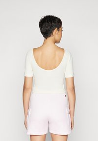 Lys ribbet kortermet topp i krem, med vid ryggscoop-hals, parret med rosa shorts med sidelommer.
