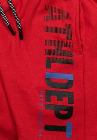 Roter Pullover mit schwarzem und blauem Text "ATHL DEPT EST 97 BKLYN", mit kontrastierenden Nähten und verstellbarem Kordelzug an der Kapuze.