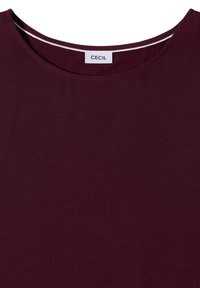 T-shirt rouge foncé à col rond avec une étiquette blanche indiquant "CECIL" cousue à l'intérieur du col au dos.