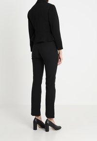 Černé sako s peplum designem, doplněné o úzké černé kalhoty. Černé vysoké podpatky dotvářejí celý outfit.