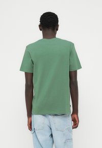 Πράσινο βαμβακερό T-shirt με κοντά μανίκια και στρογγυλή λαιμόκοψη, με λεία υφή και άνετη εφαρμογή. Χωρίς εμφανή λογότυπα ή σχέδια.