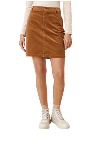 Brun kordflod mini kjol med knappstängning fram, två sidofickor och en figurnära design. Bärs med vita platå sneakers.