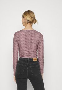 Top justo de manga longa em bordô com um padrão de estampa de leopardo. Combinado com jeans pretos de cintura alta com bolsos traseiros e uma etiqueta bege.