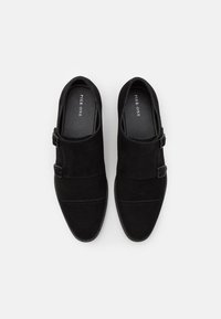 Chaussures slip-on en daim noir à profil bas, présentant un design élégant à double boucle et des détails de couture subtils.