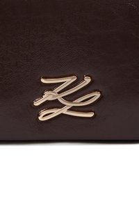 Braune Kunstledertasche mit strukturierter Oberfläche und einem auffälligen goldenen Logo-Element. Das Design ist sleek und modern.