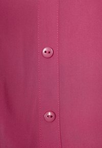 Vaaleanpunainen kangas, jossa on kaksi nappia vierekkäin, sileällä pinnalla ja samansävyisellä langalla. Napit ovat pyöreitä ja niiden keskellä on reiät.