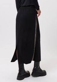 Zwarte midirok met een zijsplit en gestreepte details langs de zijkant. Gemaakt van een zachte stof, met een elastische tailleband en gecombineerd met zwarte laarzen.