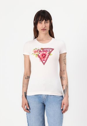 T-shirt à manches courtes blanche avec un design floral triangulaire et "GUESS ?" en rouge avec des accents de sequins sur le devant. Matériau en coton texturé.