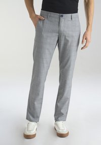 Szare spodnie w kratę o slim fit, wykonane z lekkiego materiału. Posiadają zapięcie na guzik i przednie kieszenie, zestawione z białymi sneakersami.