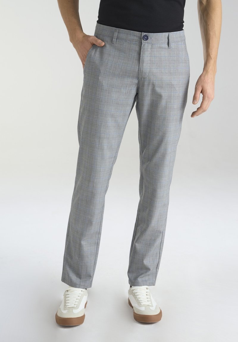 Szare spodnie w kratę o slim fit, wykonane z lekkiego materiału. Posiadają zapięcie na guzik i przednie kieszenie, zestawione z białymi sneakersami.