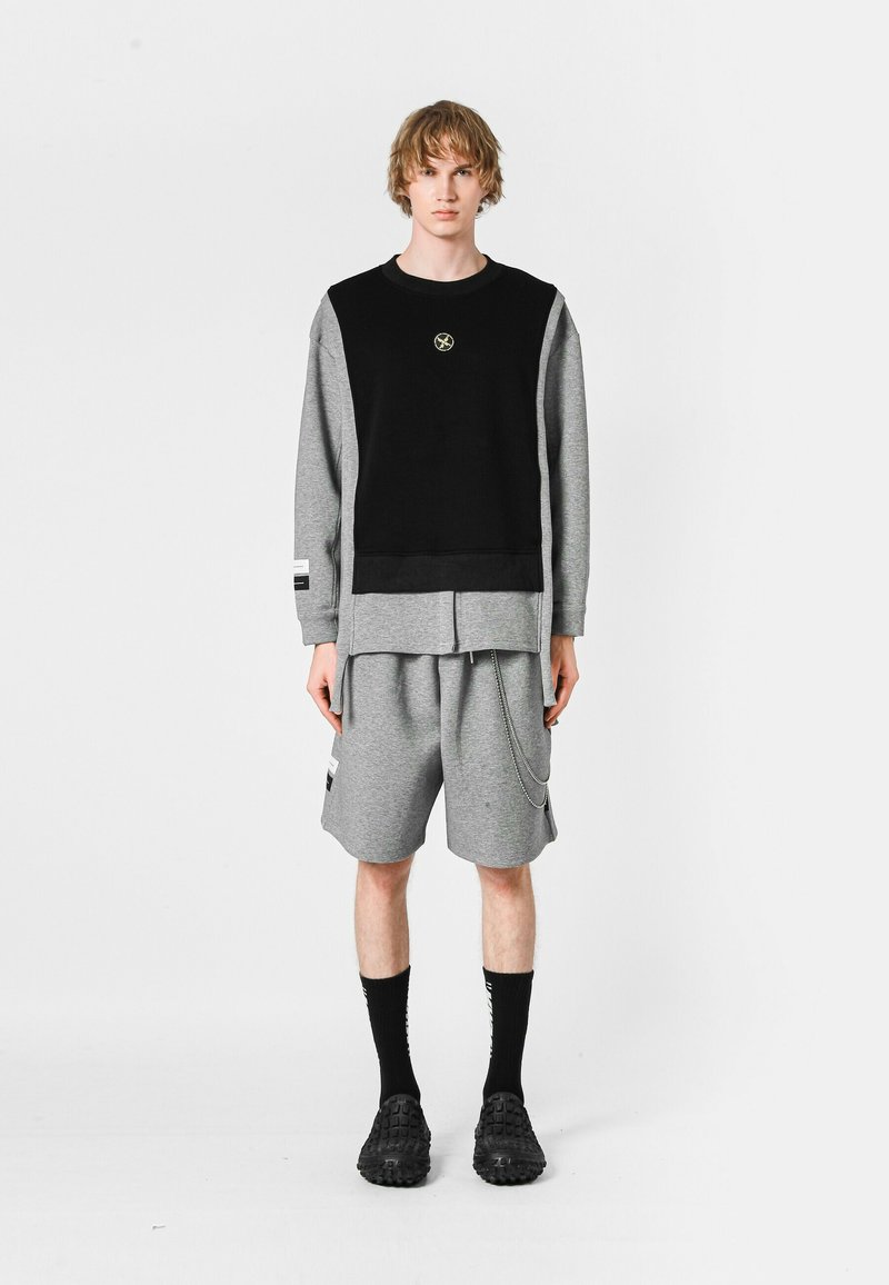 Sudadera negra y gris con paneles laterales, pantalones cortos grises con un detalle de cadena y zapatos negros; diseño minimalista, material de algodón.
