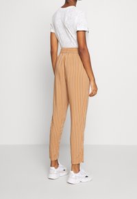 Pruhované béžové tepláky se stažitelným pasem a zúženými manžetami, v kombinaci s strukturovaným bílým tričkem a bílými teniskami.