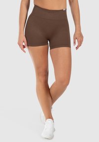 Bruine, rekbare shorts met een hoge tailleband. Gladde textuur en een aansluitend ontwerp dat tot aan het midden van de dij reikt. Gecombineerd met witte sportschoenen.