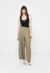 Svart ribbestrikket tank topp med scoop-hals, khaki vide bukser og beige åpne tå-mules med logo på stroppen.