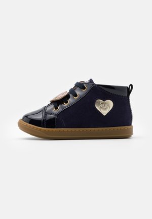 Chaussure bébé montante bleu marine avec semelle marron, lacets noirs, bout brillant et emblème cœur doré sur le côté.