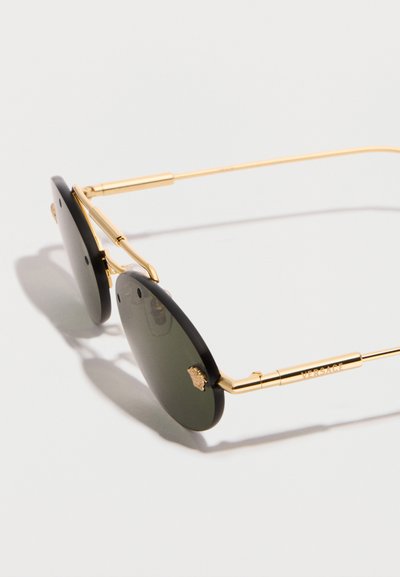 Οβάλ μαύρα γυαλιά ηλίου με λεπτά χρυσά πλαίσια, μικρό λογότυπο Medusa στους φακούς και την επιγραφή «Versace» στο πλευρικό μπράτσο.