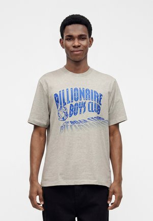 Ung mand iført en lysegrå T-shirt med blå "Billionaire Boys Club" tekst og astronaut-hjelm grafik på en ensfarvet hvid baggrund.