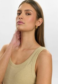 Beige ribbed tank top with wide straps, showcasing a smooth texture. Gold hoop earrings, straight brown hair, and a neutral background.