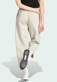 Beige Jogginghosen mit lockerer Passform, elastischem Bündchen und Seitentasche. Getragen mit weißen Sneakers, die eine strukturierte schwarze Laufsohle haben.