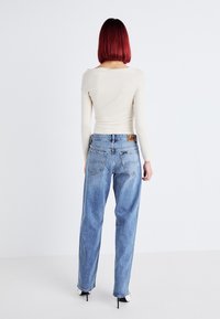 Beige langemouwen top en lichtblauwe high-waisted jeans met een leren Lee-logo op de tailleband. Slanke mouwen en recht gesneden broekspijpen.
