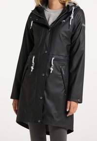 Imperméable noir avec capuche, accents argentés, détails à cordon, boutons-pression et poches latérales. Fini lisse et mat.