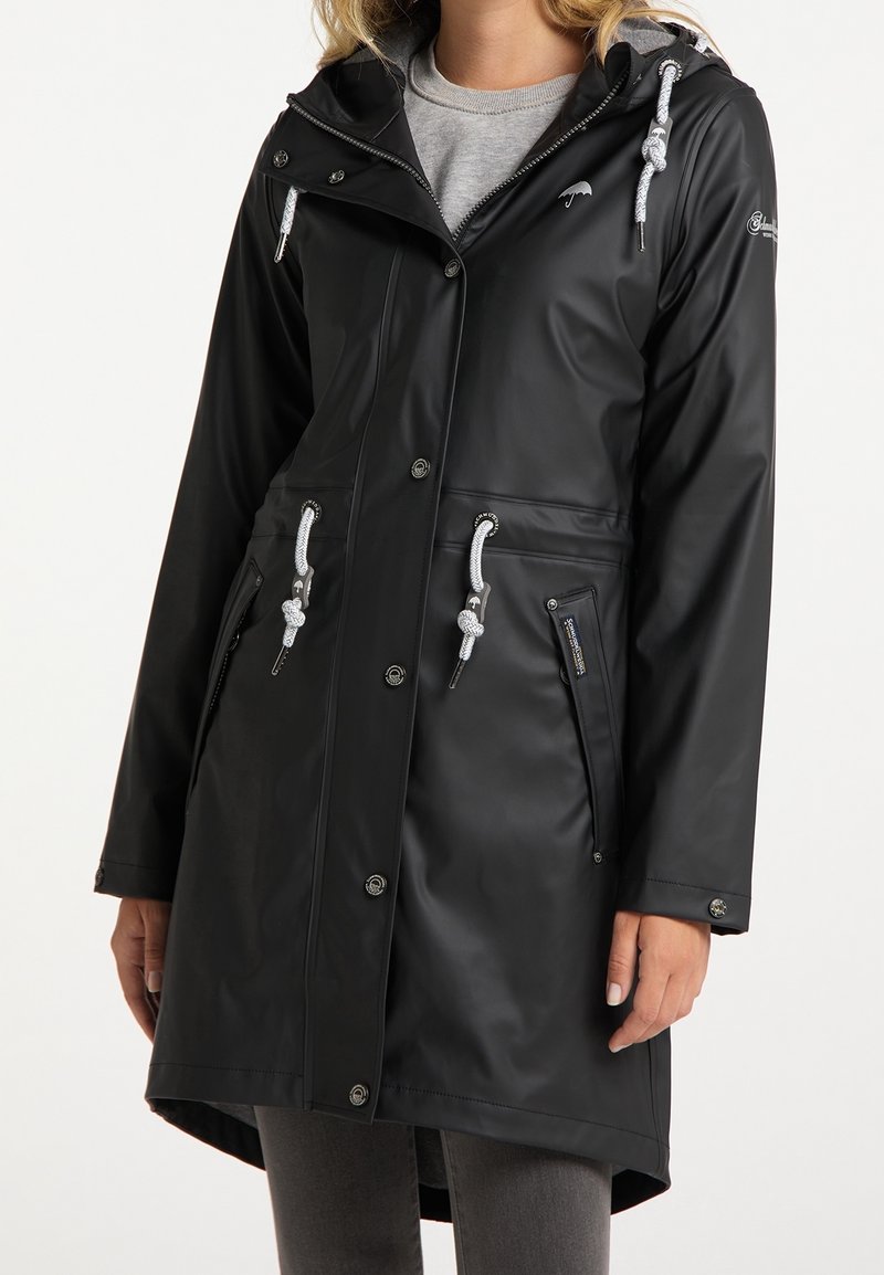 Imperméable noir avec capuche, accents argentés, détails à cordon, boutons-pression et poches latérales. Fini lisse et mat.
