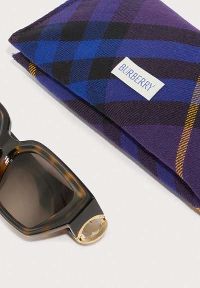 Occhiali da sole tartaruga con lenti scure accanto a una custodia a motivo a scacchi viola e blu con etichetta bianca "BURBERRY".