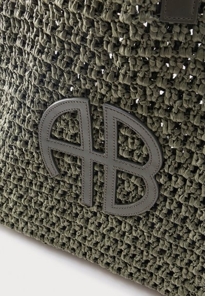 Υφασμα σκούρου πράσινου χρώματος με ανάγλυφο, ραμμένο λογότυπο από δέρμα που απεικονίζει στυλιζαρισμένα, επικαλυπτόμενα γράμματα "A" και "B".