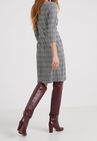 Robe grise à carreaux avec manches trois-quarts, longueur mi-mollet, associée à des bottes en cuir bordeaux au-dessus du genou avec un talon épais.