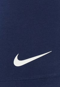 Tecido atlético azul-marinho, com uma textura suave, apresenta um prominente logótipo Nike swoosh branco. Detalhes das costuras estão visíveis.