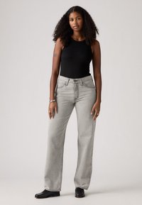 Zwarte geribbelde tanktop met grijze wijde jeans, voorzien van voorzakken en een hoge taille. Geweven stof met een gladde afwerking. Zwarte schoenen.