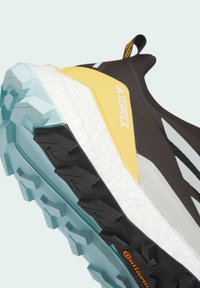 Baskets de course noires avec un dessus texturé, des accents jaunes et une semelle multicolore dotée de crampons prononcés pour une meilleure adhérence.