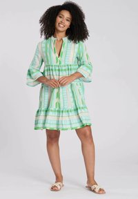 Vestido de estampado verde y blanco con escote en V, mangas acampanadas de 3/4 y falda en capas. Hecho de un tejido ligero, con diseños geométricos.