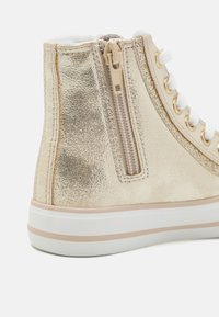 Guldmetalliska hög-top sneakers med en texturerad yta, vita snörning och en siddragkedja. Har en kontrasterande vit sula med beige ränder.