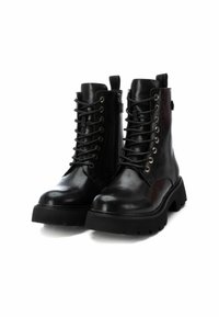 Botas de tobillo de cuero negro con cordones en la parte delantera, ojales metálicos, cremallera lateral y suela de goma gruesa. Textura suave y diseño robusto.