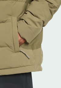 Maslinasto zelena puhasta jakna s džepom na patentni zatvarač, glatkom vanjštinom i prošivenom teksturom. Ustravljena u struku za čvrsto prianjanje.