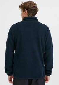Marineblaue Fleecejacke mit hohem Kragen, strukturiertem Material und Seitennähten. Verfügt über ein kleines Logo auf der linken Schulter. Lockere Passform.
