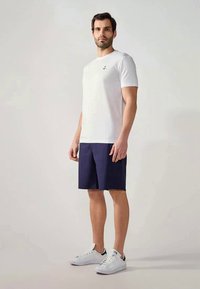 Hvid kortærmet t-shirt med et lille ankerlogo, parret med navy shorts og hvide sneakers, med et rent, enkelt design.