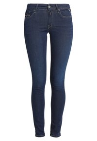 Jeans ajustados de denim azul oscuro, con un tiro medio, diseño de cinco bolsillos y costuras en contraste. Textura suave con ligero estiramiento.