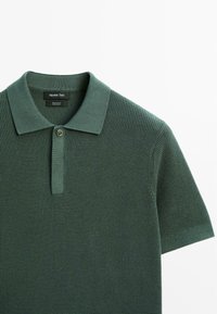 Polo shirt in cotone verde con tessuto testurizzato, dotato di colletto a patch, placca con due bottoni e maniche corte. Etichetta del marchio visibile.
