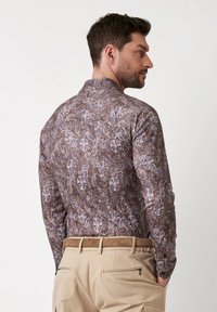 Langarmshirt in een bruine en grijze paisley-print, met een kraag en textuurstof, gecombineerd met lichtgekleurde broeken.