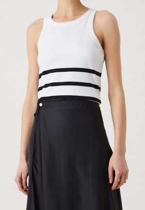 Vrouw draagt een mouwloos wit topje met twee zwarte horizontale strepen en een zwarte midi-rok met hoge taille en een zijknop.