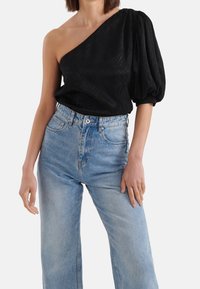 Schwarzes Top mit einem Schulterriemen aus strukturiertem Stoff und puffigem Ärmel, kombiniert mit hellblauen, hochtaillierten Jeans aus Denim.