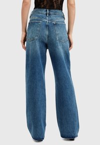Jeans de mezclilla azul de pierna ancha con cintura alta, que cuentan con grandes bolsillos traseros y un dobladillo deshilachado. La tela tiene un lavado claro y una textura suave.