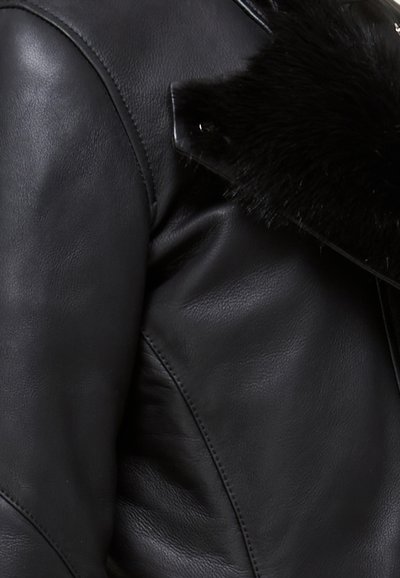 Zwart leren jack met een gestructureerd oppervlak, slank ontwerp en een zwarte bontkraag met een knoopdetail. Gladde afwerking en contournaden.