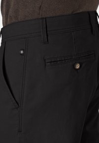 Schwarze Hose aus strukturiertem Stoff, gerade geschnitten, mit seitlichen Taschen und einer einzelnen Gesäßtasche mit Knopfverschluss. Dezentes Branding-Detail sichtbar.