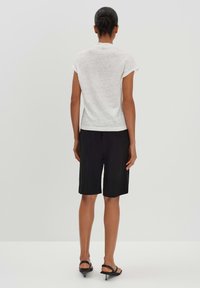 Top bianco a maniche corte con vestibilità comoda, abbinato a pantaloni corti neri fino al ginocchio. Tessuto liscio, design semplice senza motivi visibili.
