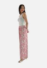 Roze bloemenpatroon wijde broek met elastische tailleband, gecombineerd met een aansluitend witte tanktop en lichtgekleurde haksandalen.