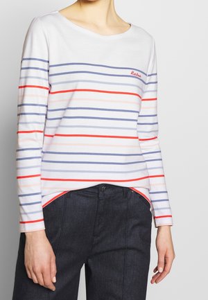 Osoba ubrana w białą koszulę z długim rękawem z poziomymi czerwonymi, różowymi i niebieskimi paskami, zestawioną z ciemnoniebieskimi spodniami z wysokim stanem.